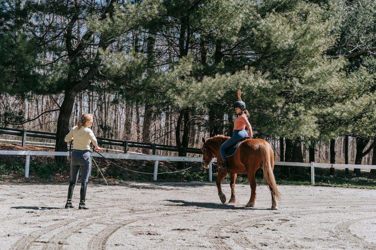 Woman instructing a child horseback riding under sunny forest trees.
